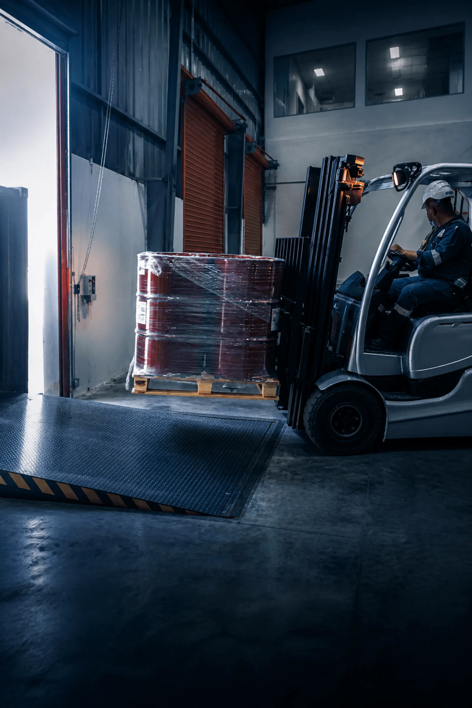 Forklift loading palletised industrial drums at a warehouse dock